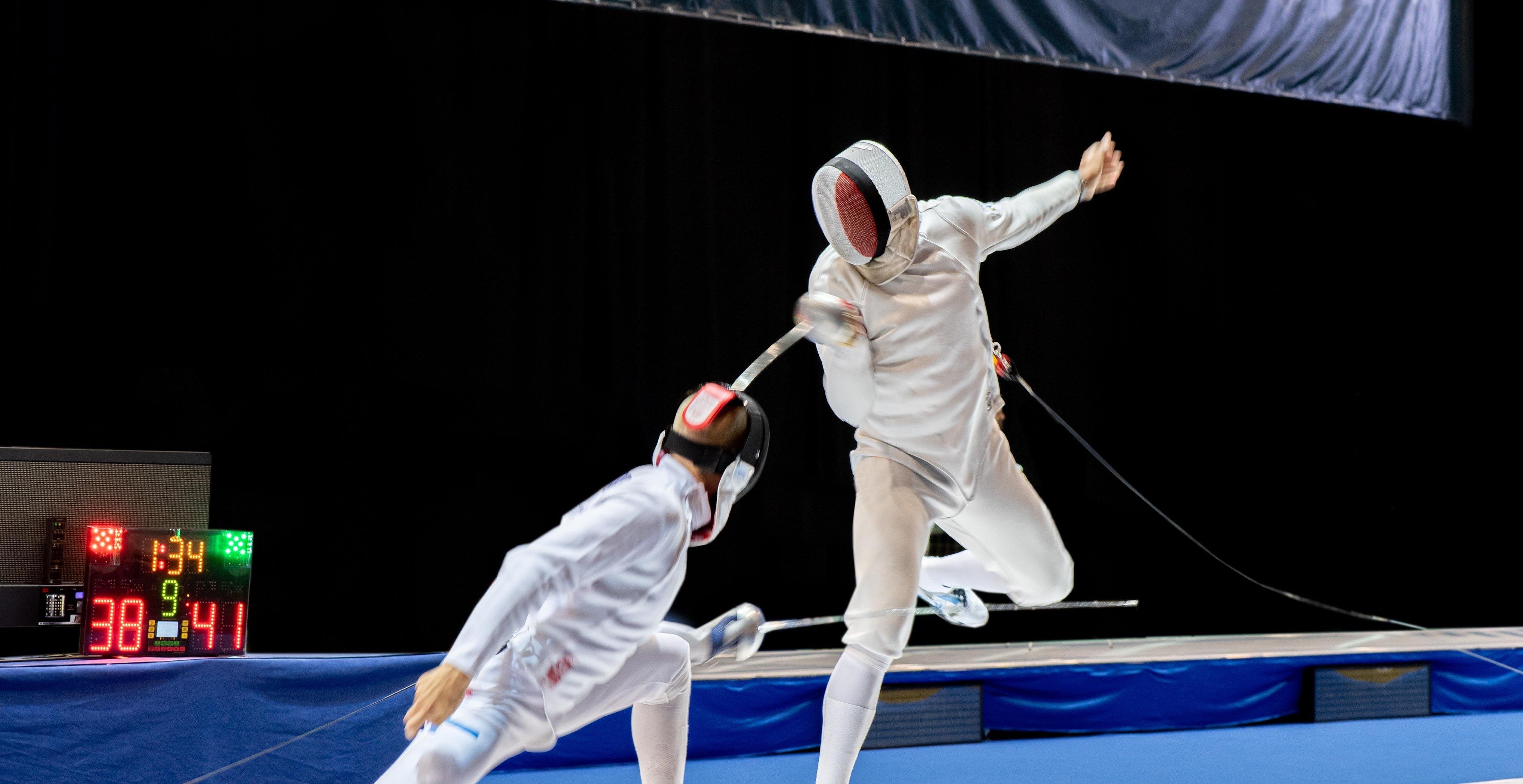 Two fencers compete on the piste, with one lunging and one dodging. 