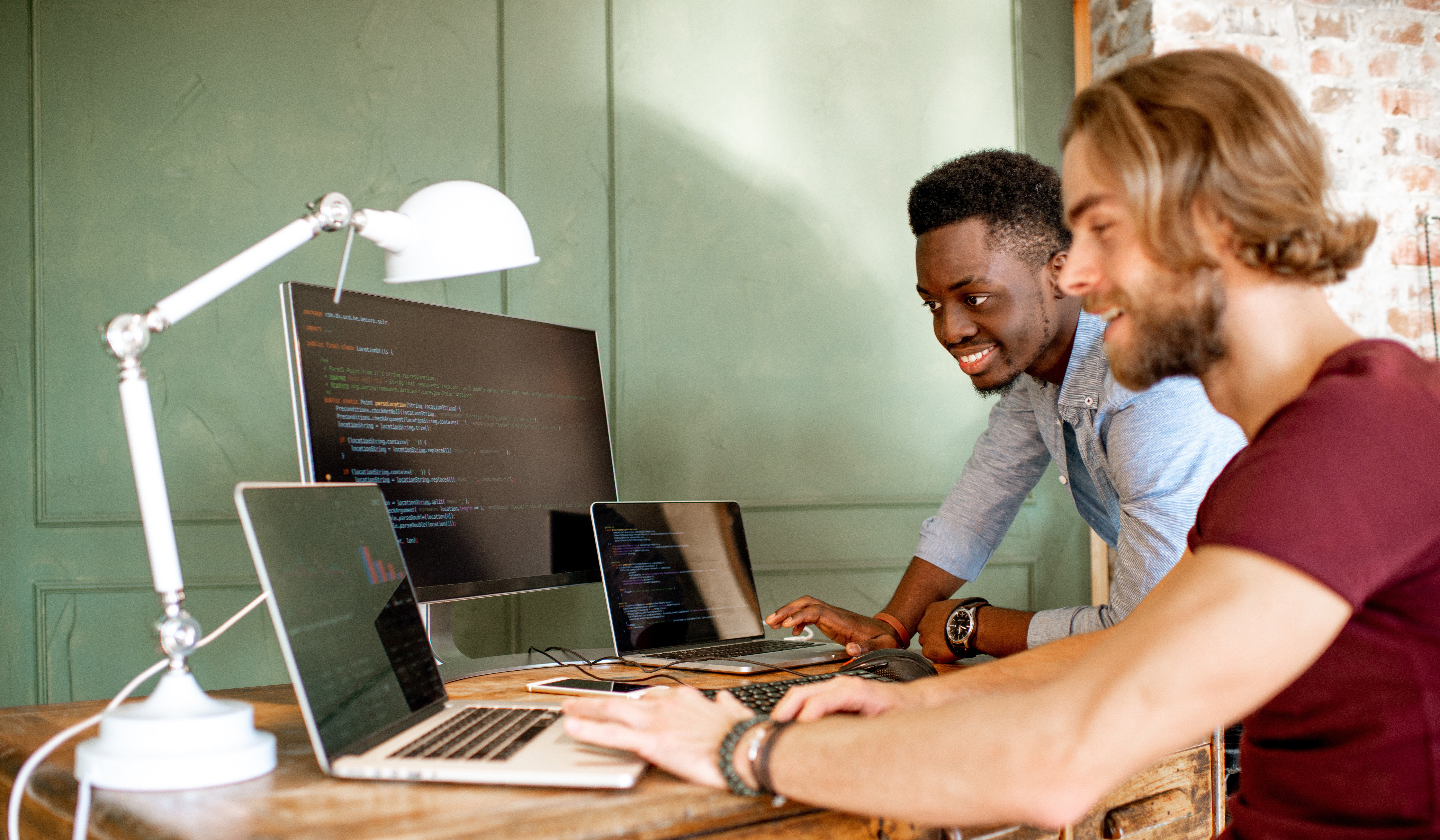 Two people using two computers and a monitor to create code