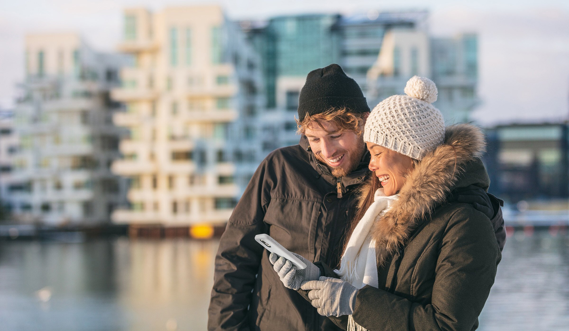 Two people looking at a phone wearing winter hats and gloves