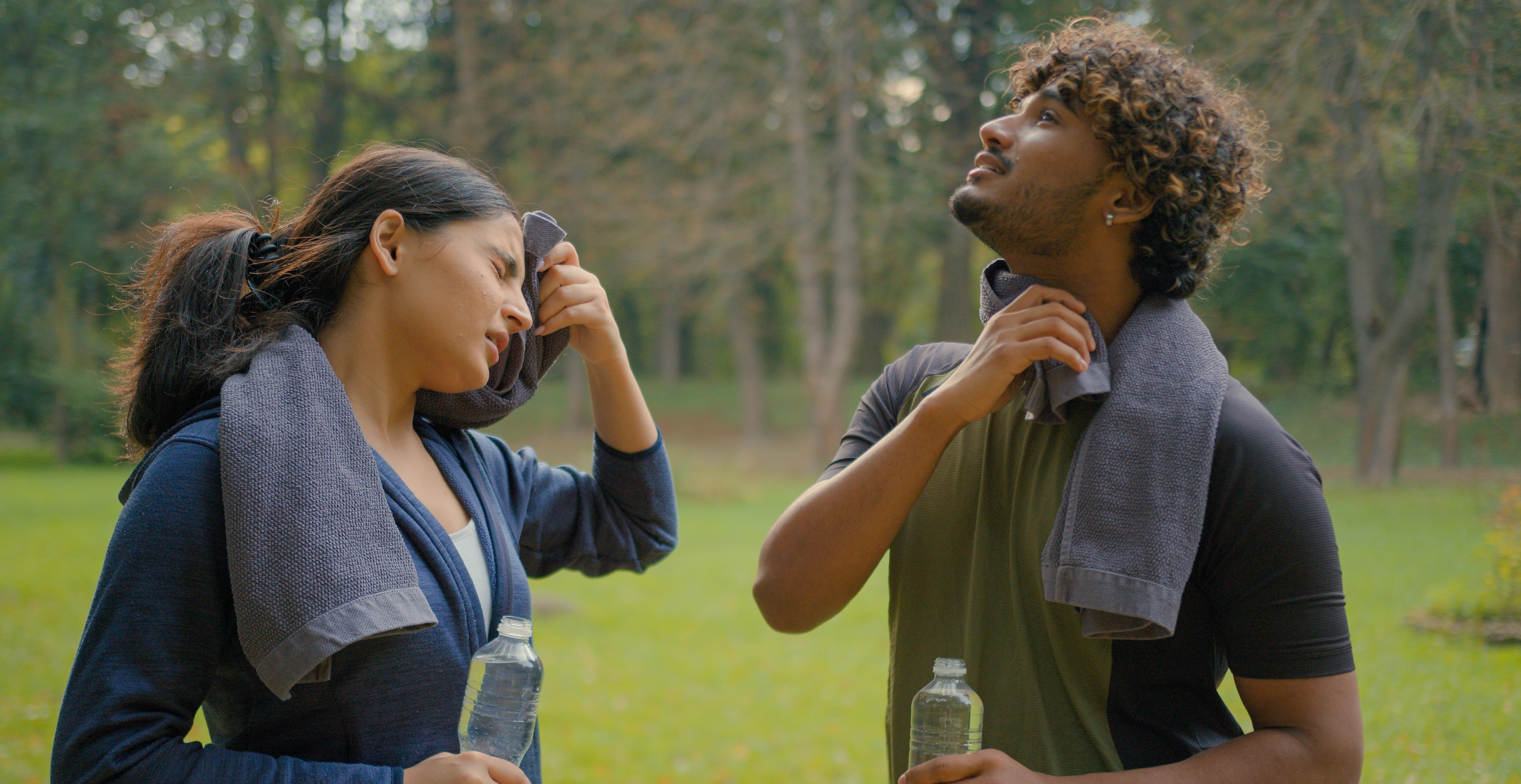 Two adults wipe away sweat with towels while standing outside. 