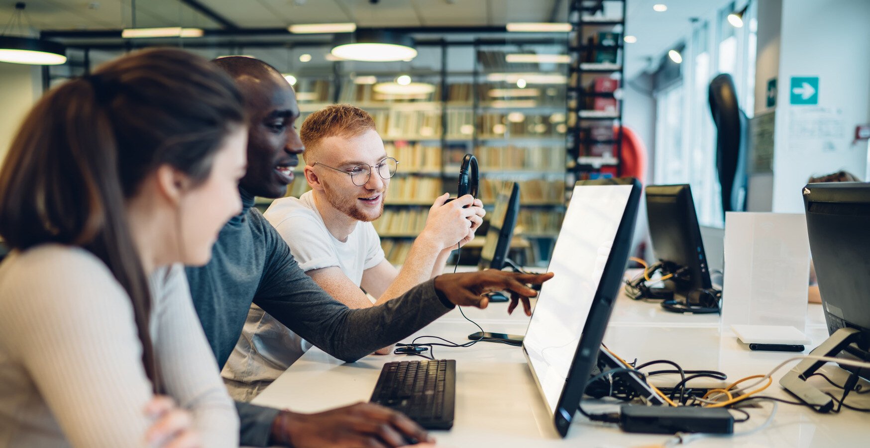 A group of three students point at a computer while having a conversation.