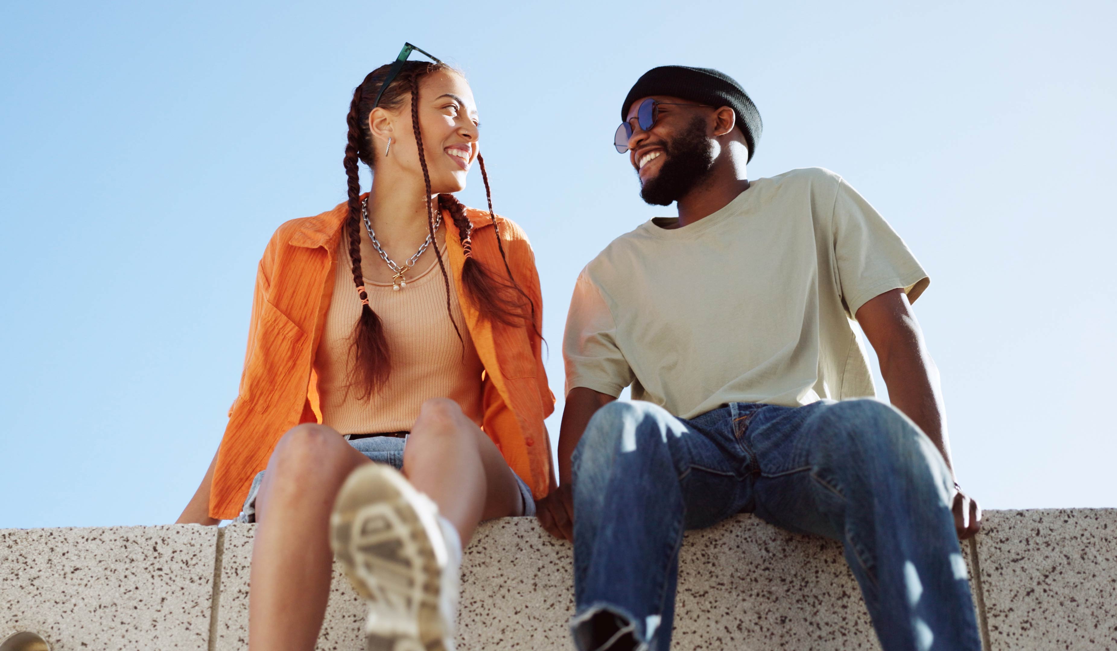 A couple sitting on a stone wall with the sky behind them